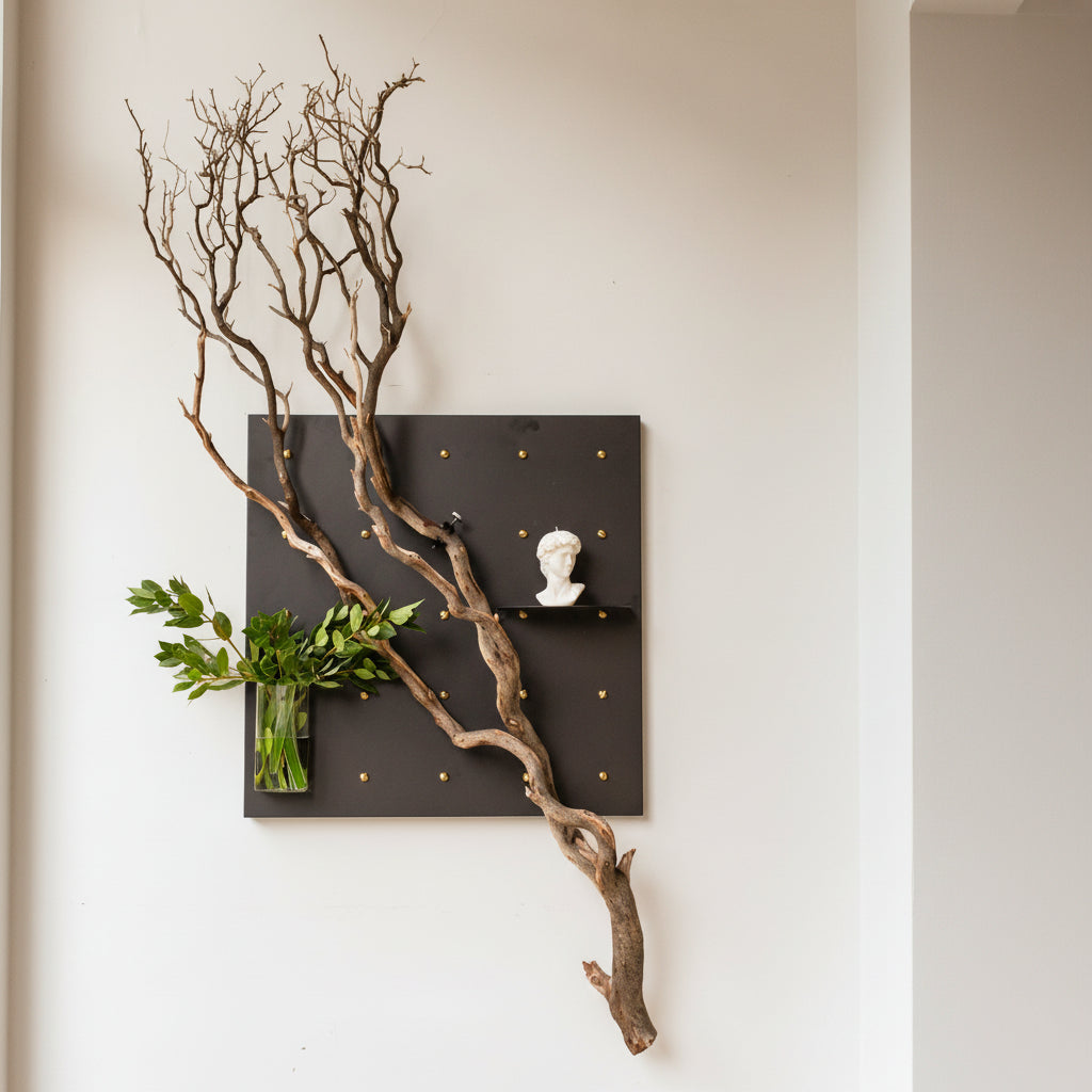 Decorative 30x30 Curator Wall Panel with branches, a vase of greenery, and a bust on a black board against a light gray wall.